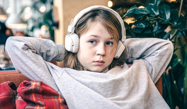 Uma menina bonitinha está sentada no sofá usando fones de ouvido