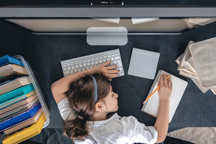 Foto grátis uma menina cansada deita-se em uma mesa na frente de um computador com cadernos e livros