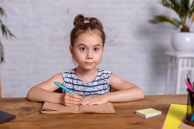 Uma menina criança fazendo lição de casa escrevendo e lendo em casa. Menina escreve em um caderno sentado à mesa