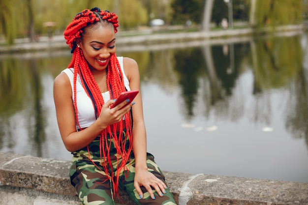 Uma menina de pele escura nova e elegante com dreads vermelho que anda no parque do verão perto do rio