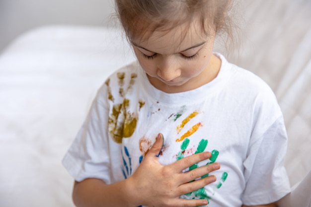 Foto grátis uma menina deixa vestígios de palmas das mãos pintadas em uma camiseta. criatividade e arte infantil.