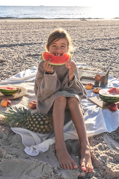 Uma menina em uma praia de areia do mar come uma melancia