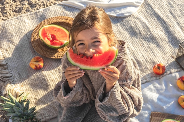 Uma menina em uma praia de areia do mar come uma melancia