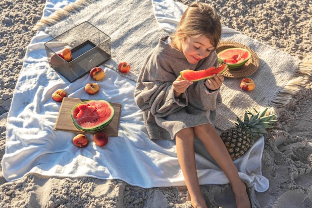 Uma menina em uma praia de areia do mar come uma melancia