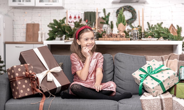 Uma menina gosta de muitos presentes de Natal sentada no sofá em casa