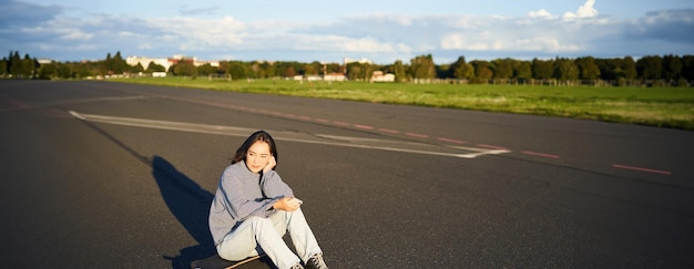 Foto grátis uma menina patinadora senta-se em seu skate na estrada usando um smartphone conversando em um aplicativo móvel