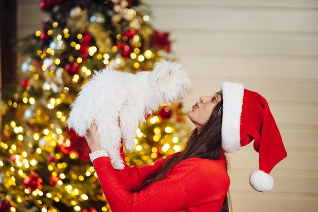 Uma menina segura um cachorrinho nas mãos na árvore de Natal