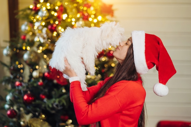 Uma menina segura um cachorrinho nas mãos na árvore de Natal
