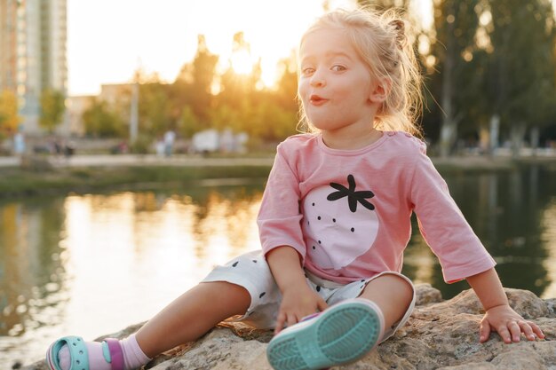 Uma menina sentada em uma pedra enorme no parque perto do lago