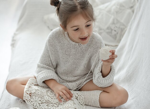 Uma menina sentada no sofá e aprendendo a tricotar, o conceito de lazer em casa.