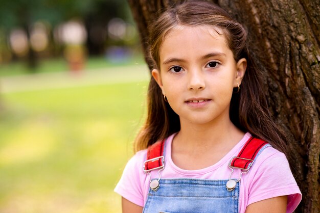 Uma menina sentada perto de uma árvore, olhando para a câmera