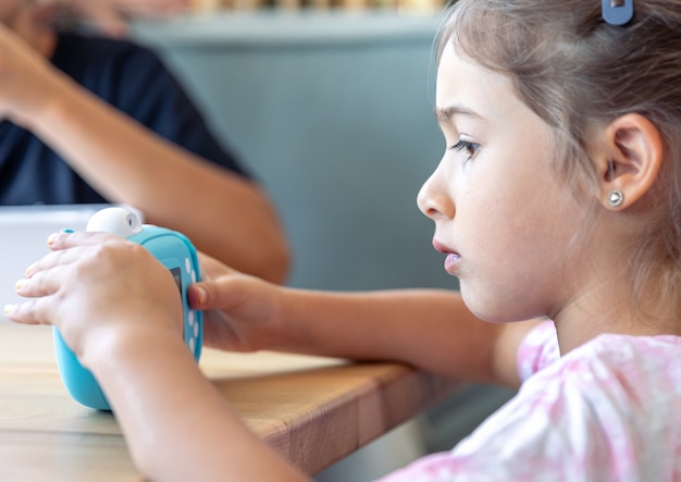 Uma menina tem nas mãos uma câmera digital de brinquedo azul para crianças para impressão instantânea de fotos.