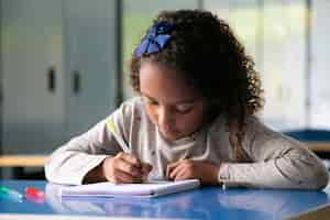Foto grátis uma mistura focada em uma corrida de garota sentada na mesa da escola e desenhando no caderno