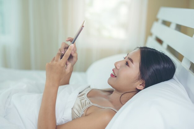 Uma mulher asiática bonita relaxa e trabalha com um computador portátil, lendo em casa.