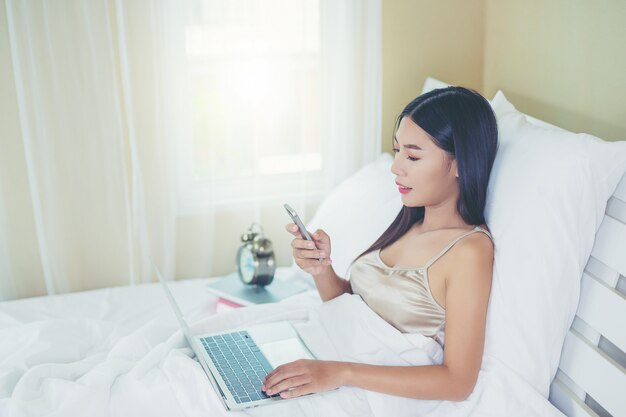 Uma mulher asiática bonita relaxa e trabalha com um computador portátil, lendo em casa.