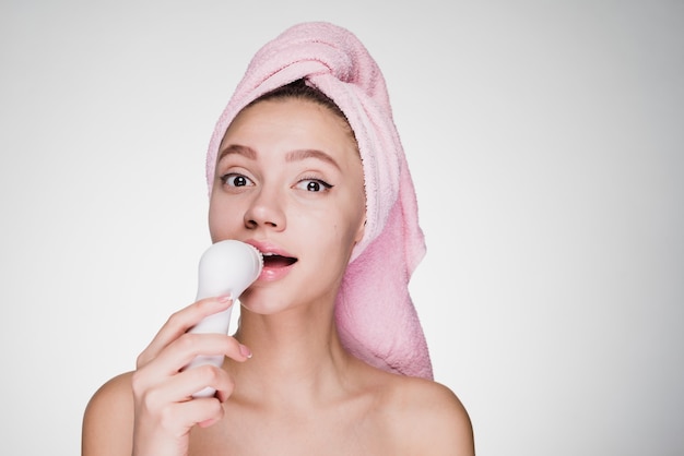Uma mulher atenciosa com uma toalha na cabeça após o banho limpa o rosto com uma escova para uma limpeza profunda