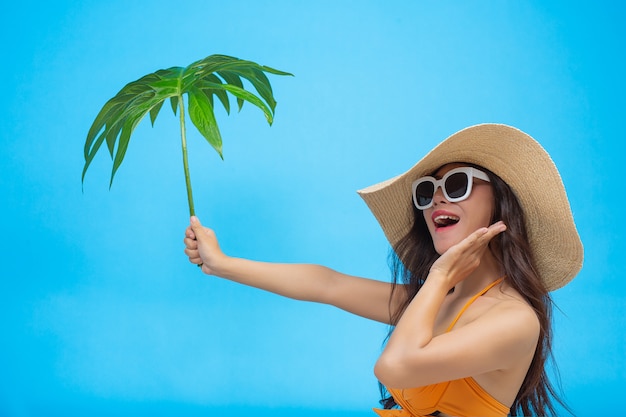 Uma mulher bonita em um maiô segurando uma folha verde coloca no azul