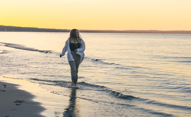Uma mulher caminha ao longo do mar com os pés descalços no espaço da cópia do pôr do sol