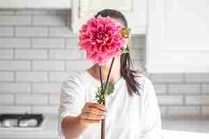 Foto grátis uma mulher cobre o rosto com uma flor de dahlia rosa em um fundo interior branco