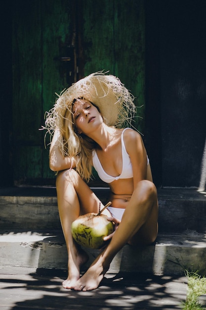 Uma mulher com um chapéu de palha bebe um coco tropical