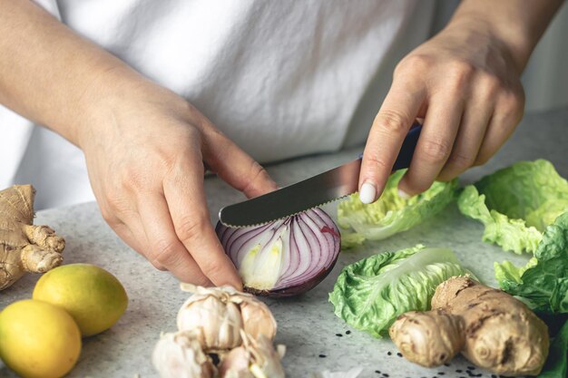 Foto grátis uma mulher corta cebolas para salada na mesa da cozinha em close-up