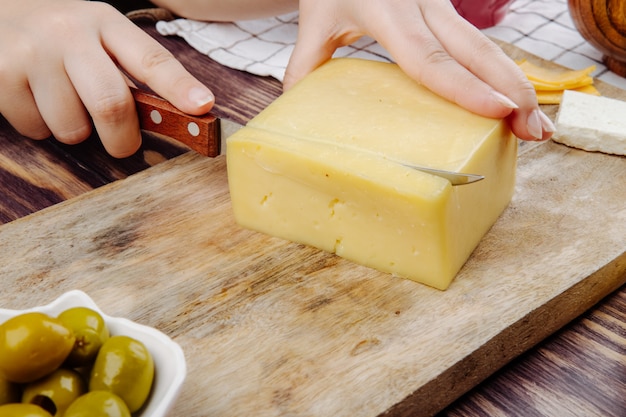 Uma mulher corta queijo holandês em uma placa de madeira vista lateral