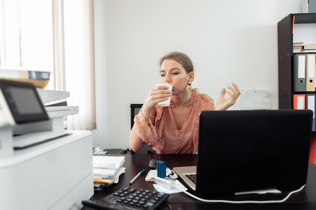 Uma mulher de negócios atraente bebe café em seu local de trabalho no escritório coffee break Foto Premium