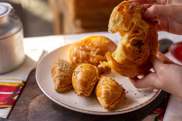 Uma mulher de pastelaria vista frontal rasgando qogal junto com outras padarias biscoitos hora do chá saborosa cerimônia de massa de pão na mesa