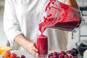 Foto grátis uma mulher derrama um smoothie de frutas vermelhas do liquidificador em um copo