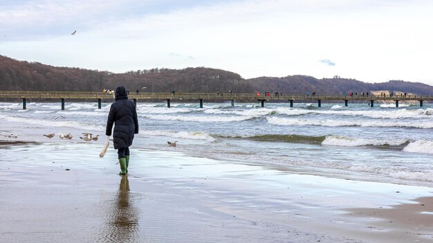 Uma mulher em uma jaqueta de inverno e botas caminha à beira-mar
