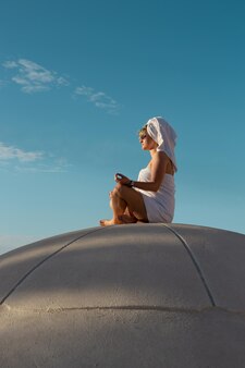 Uma mulher em uma toalha meditando e cumprimentando a manhã no telhado de um edifício esférico