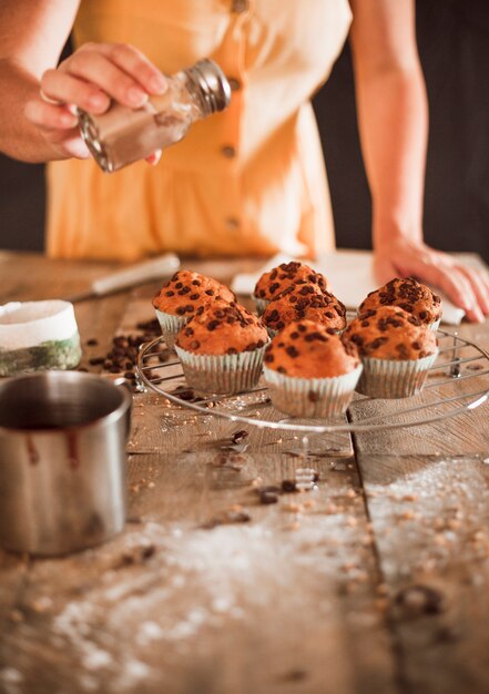 Uma mulher espanando cacau em pó em muffins caseiros em rack de arrefecimento