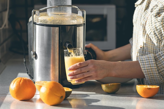 Uma mulher faz suco de laranja em casa na cozinha com um espetador elétrico