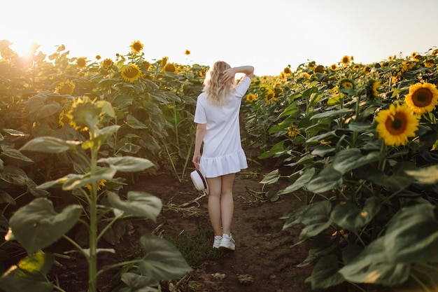 Uma mulher loira com um vestido branco no campo com girassóis