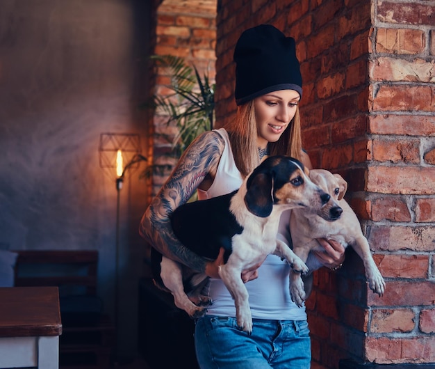 Uma mulher loira tatuada elegante em t-shirt e jeans detém dois cães fofos.