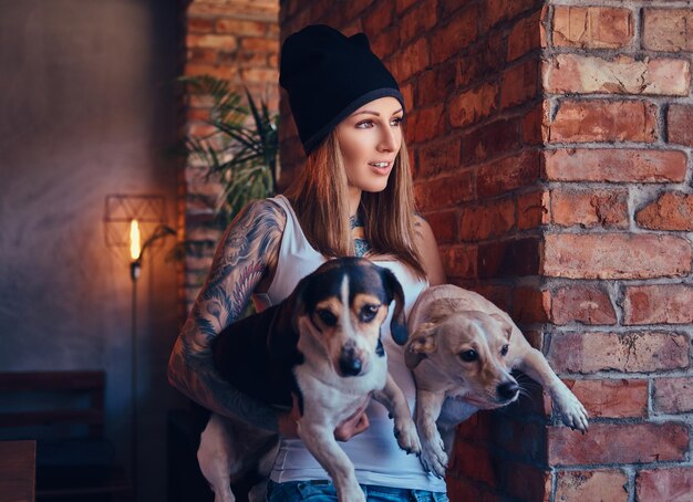 Uma mulher loira tatuada elegante em t-shirt e jeans detém dois cães fofos.