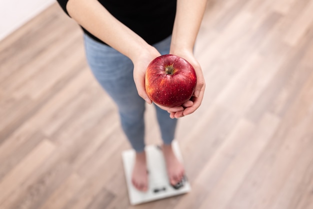 Uma mulher mede peso em uma balança com uma maçã nas mãos