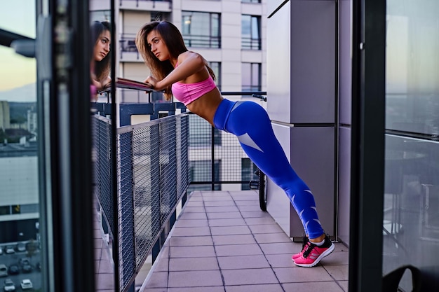 Foto grátis uma mulher morena flexível vestida com roupas esportivas fazendo exercícios na varanda.