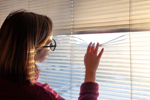 Uma mulher olha através das cortinas para a luz do sol da manhã