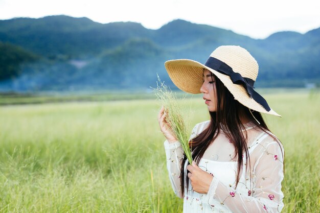 Uma mulher que está segurando uma grama nas mãos em um belo campo de grama com uma montanha.
