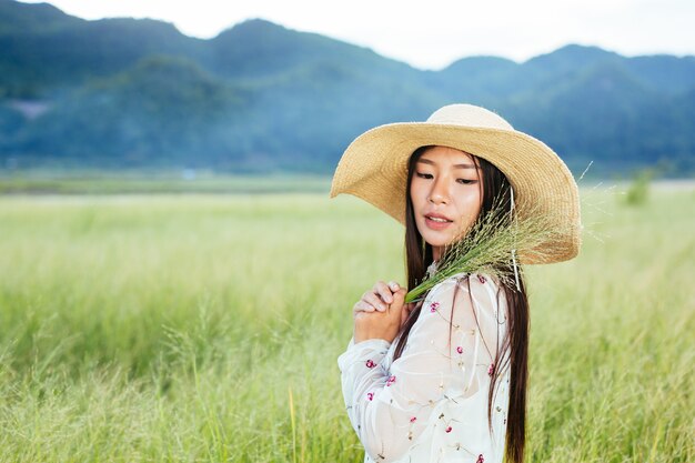 Uma mulher que está segurando uma grama nas mãos em um belo campo de grama com uma montanha.