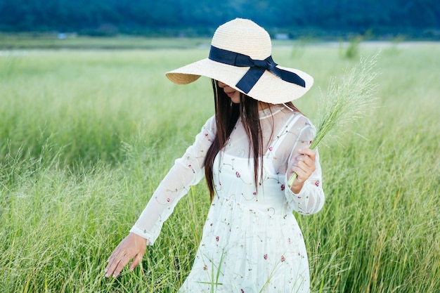 Uma mulher que está segurando uma grama nas mãos em um belo campo de grama com uma montanha.