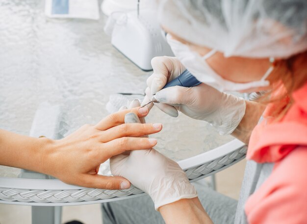 Uma mulher recebendo manicure de uma mulher em luvas e máscara no salão de beleza durante o dia