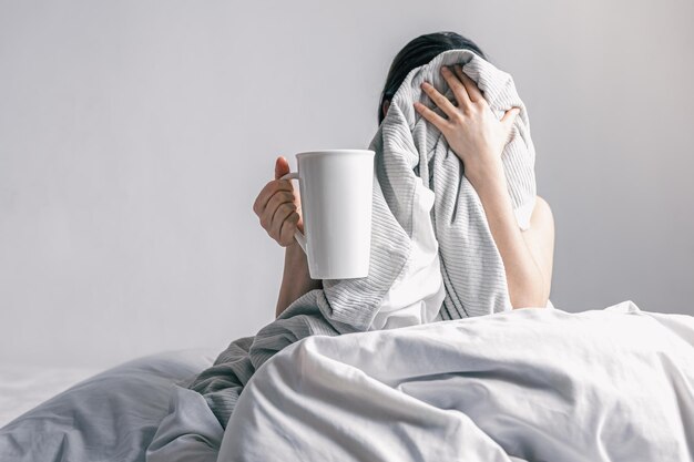 Uma mulher segura uma xícara de café enquanto está deitada na cama