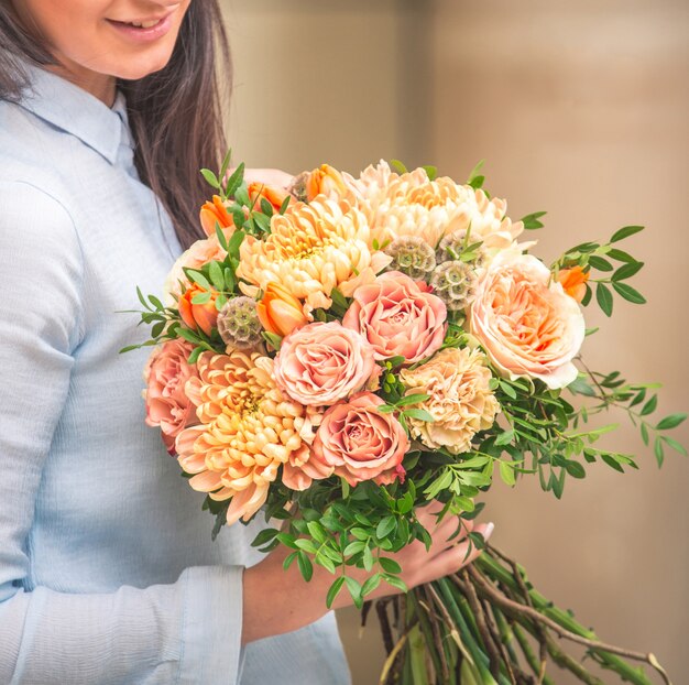 Uma mulher segurando um buquê de rosas corais e peônias na mão