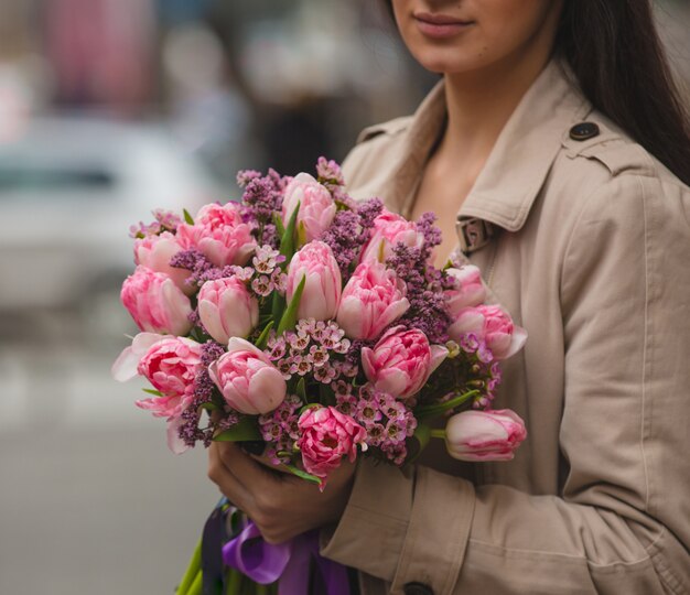 Uma mulher segurando um buquê de tulipas cor de rosa uma sirene na mão