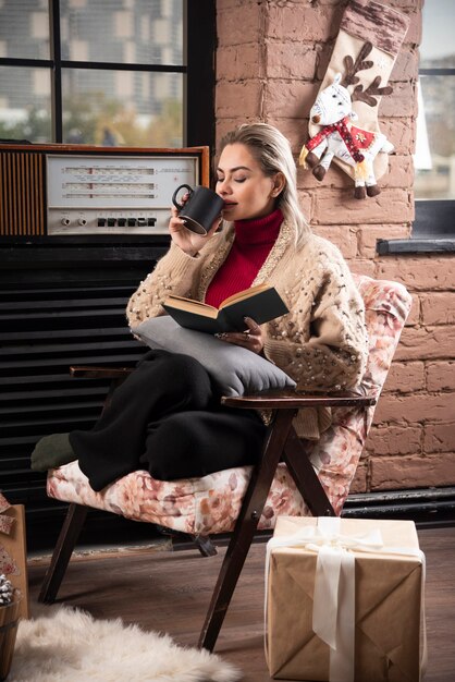 Uma mulher sentada, lendo um livro e tomando café