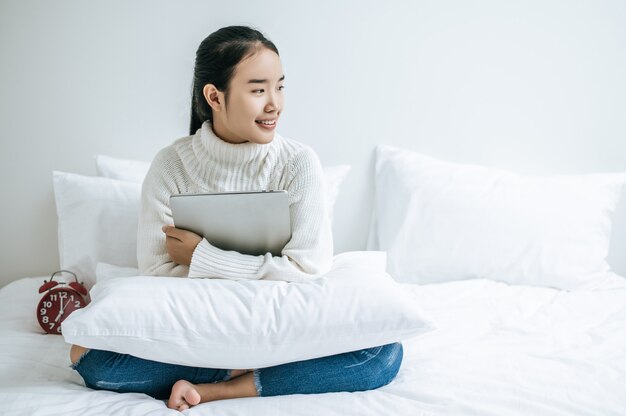 Uma mulher sentada na cama, abraçando o laptop e sorrindo.