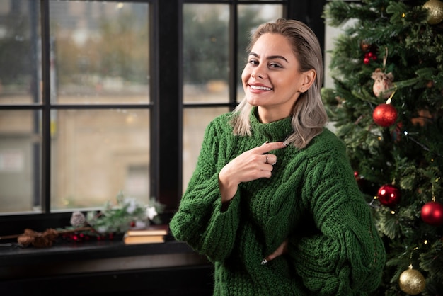 Foto grátis uma mulher sorridente, vestindo um suéter verde, se passando perto da árvore de natal.