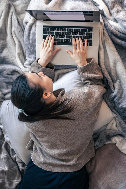 Uma mulher trabalhando em um laptop enquanto estava deitada na cama vista superior